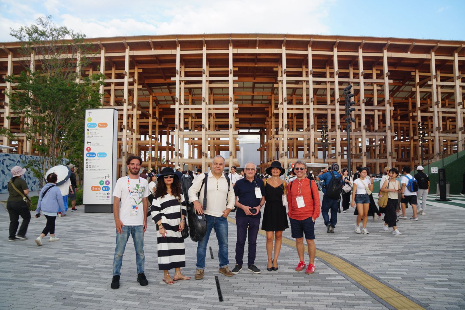 Gruppo di persone davanti a una struttura in legno moderna e trafficata con cielo sereno e visitatori intorno.