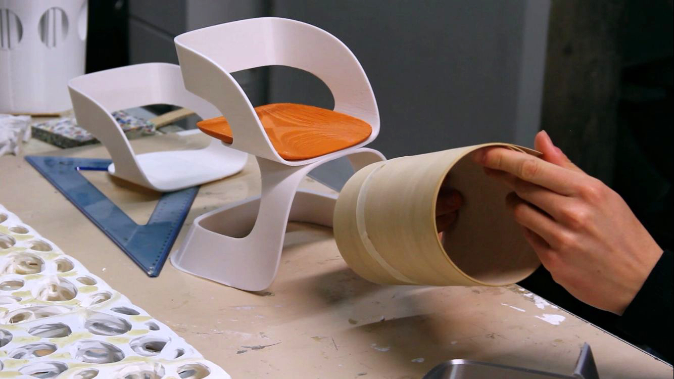 Designer crea modelli di sedie in miniatura su tavolo da lavoro con strumenti e materiali.