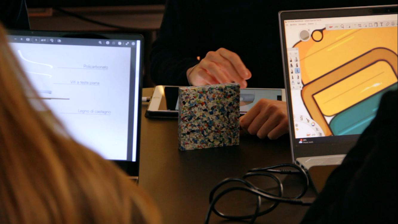 Persone al lavoro su laptop e tablet in ufficio, concentrati su progetti grafici e design.