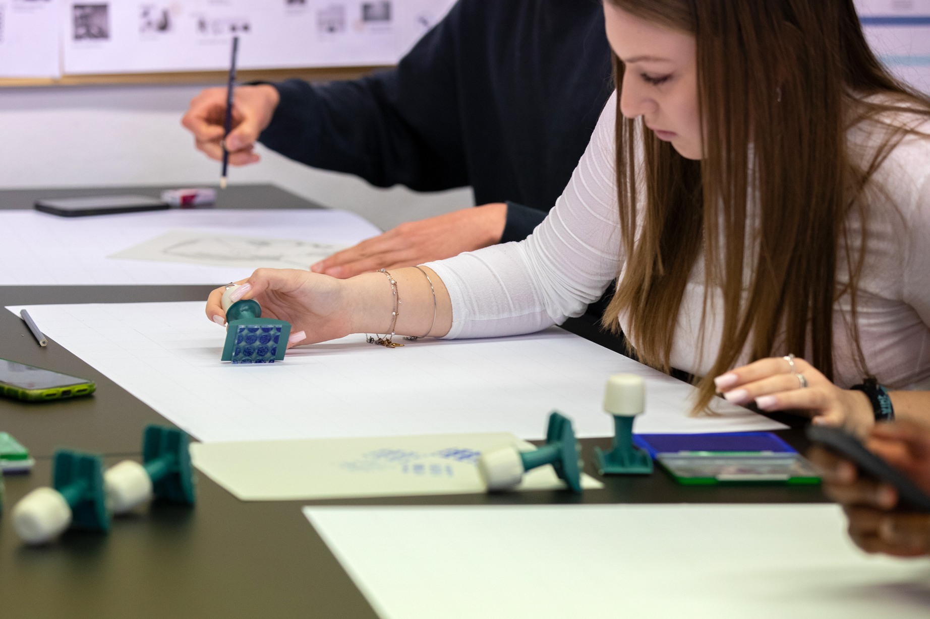 Studentessa crea disegni con timbri su carta bianca al tavolo, focus su creatività e apprendimento artistico.