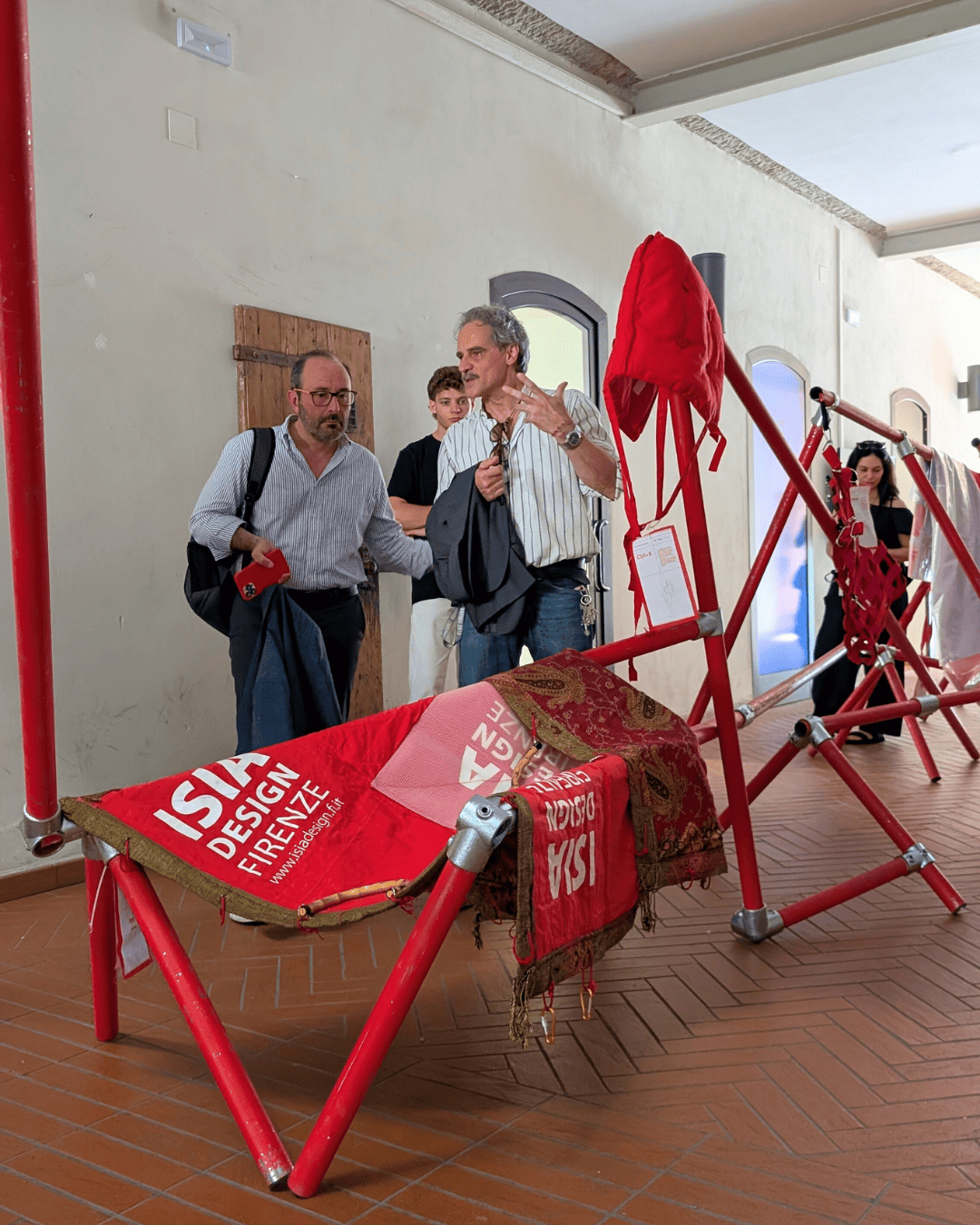 Persone osservano una struttura di design rosso esposta in una mostra d'arte a Firenze.