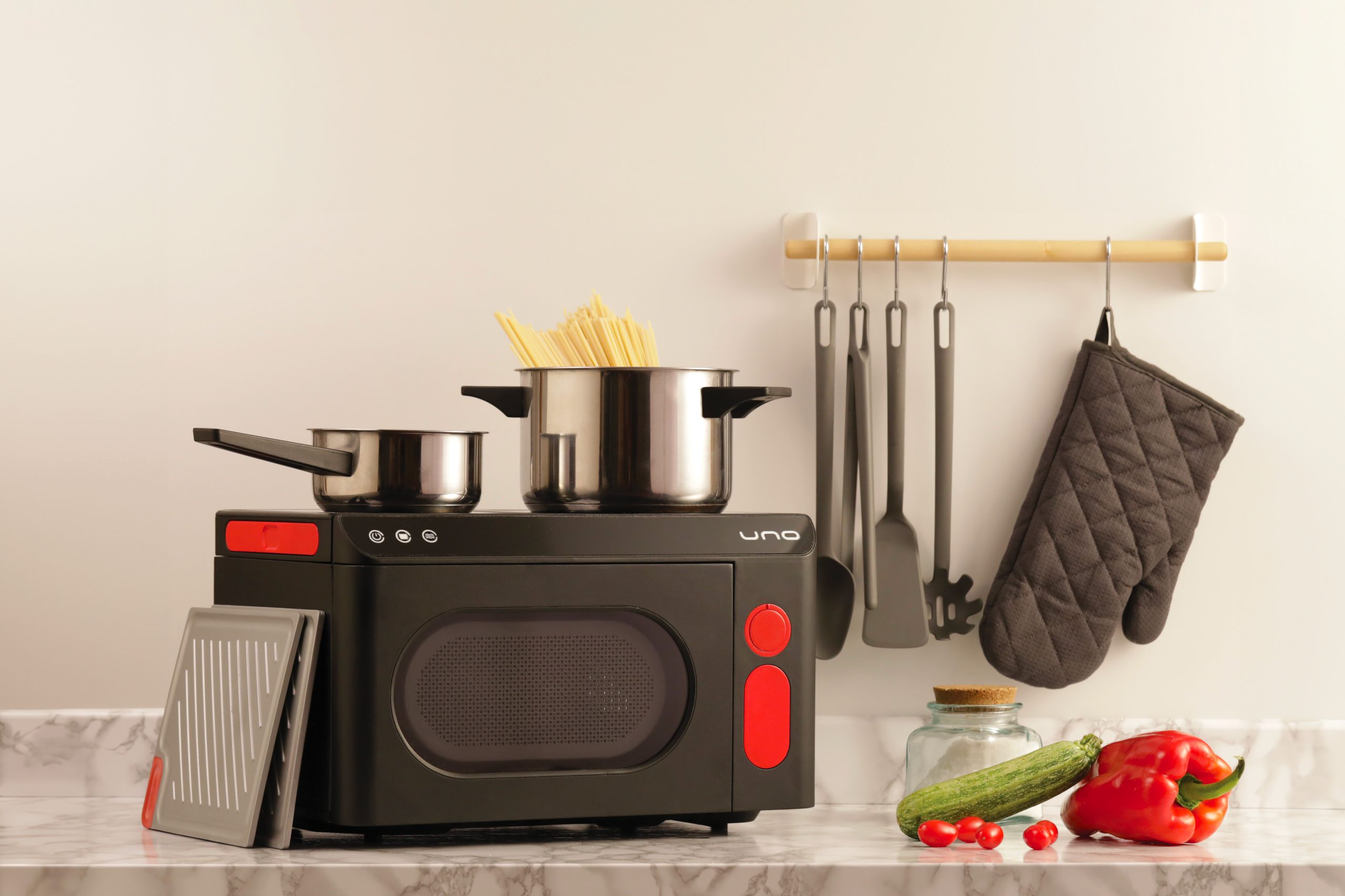Mini cucina moderna con pentole e utensili, ortaggi freschi su marmo, ambiente domestico elegante.