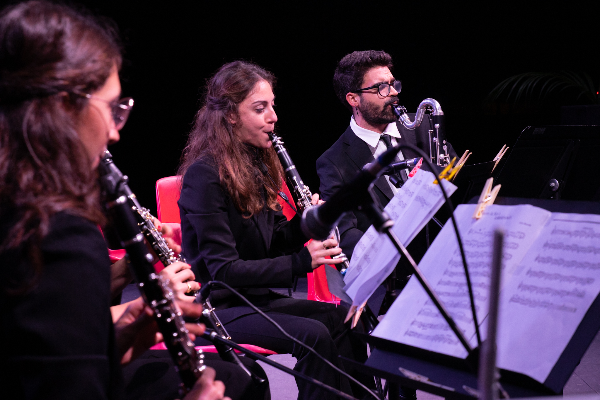 Musicisti suonano i clarinetti in un'orchestra, concentrati sulle partiture sul leggio.
