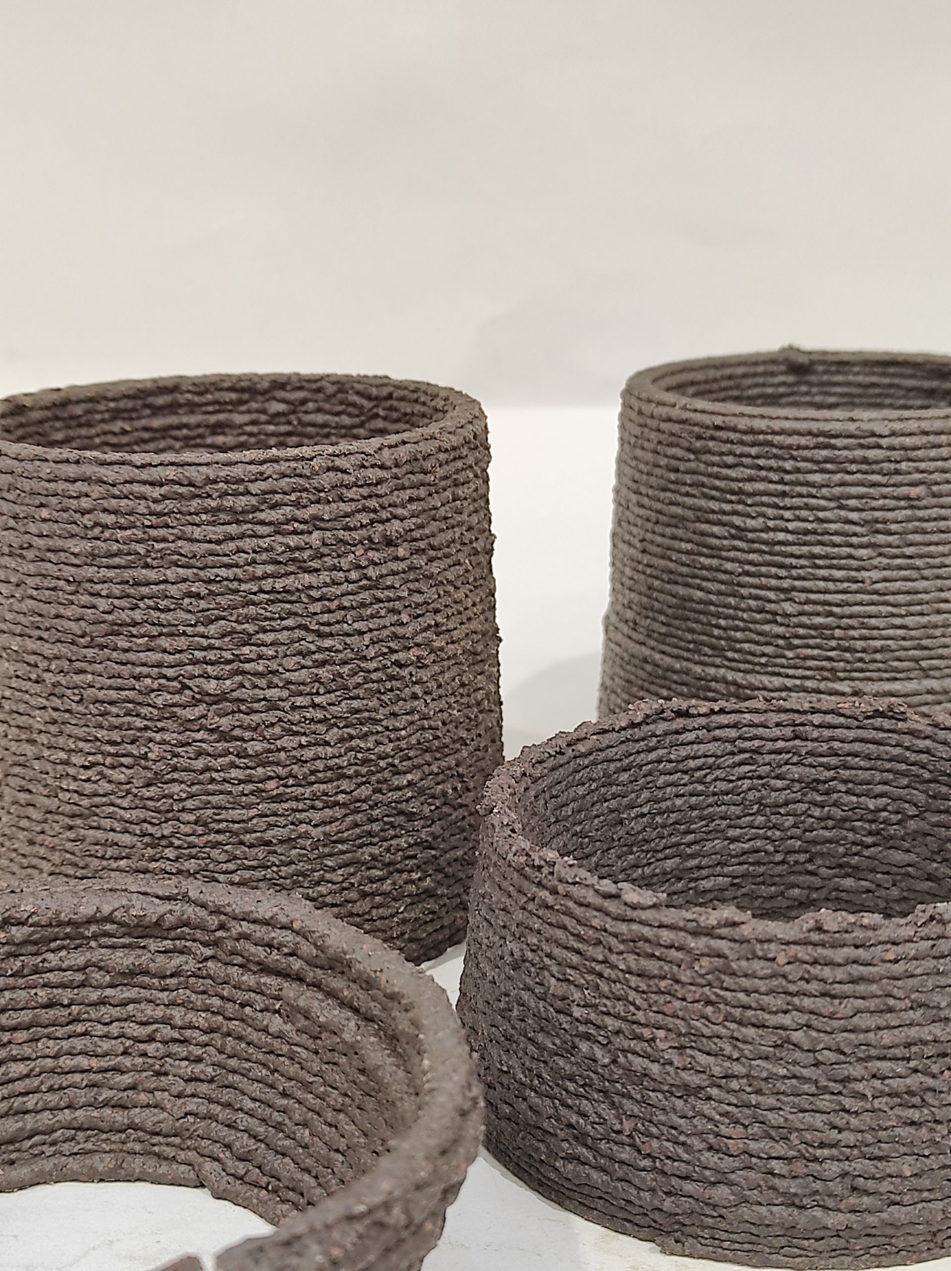 Vasi in terracotta tessuta, texture naturale e colori terrosi, su sfondo chiaro.