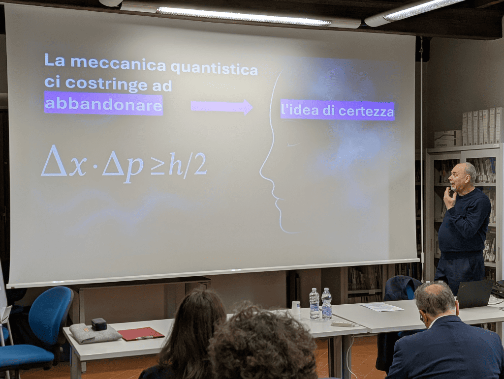 Presentazione sulla meccanica quantistica e incertezza con relatore accanto a schermo con testo ed equazione scientifica.
