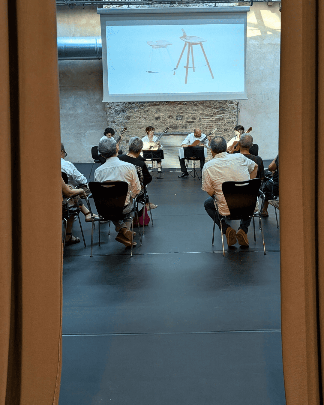 Persone assistono a una presentazione con chitarre e proiettore in una sala conferenze.