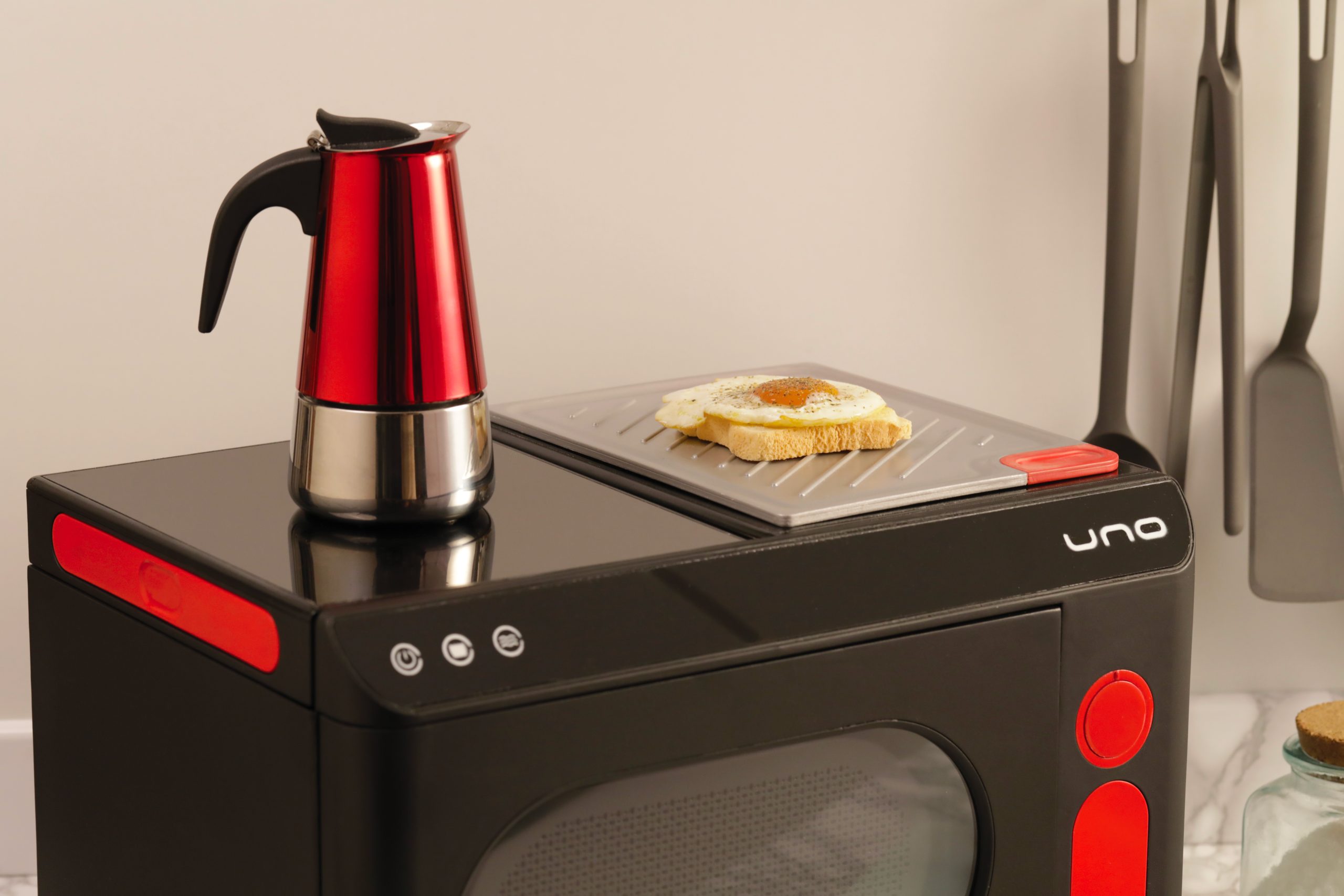 Caffettiera rossa e pane tostato con uovo su un elettrodomestico nero in cucina moderna.