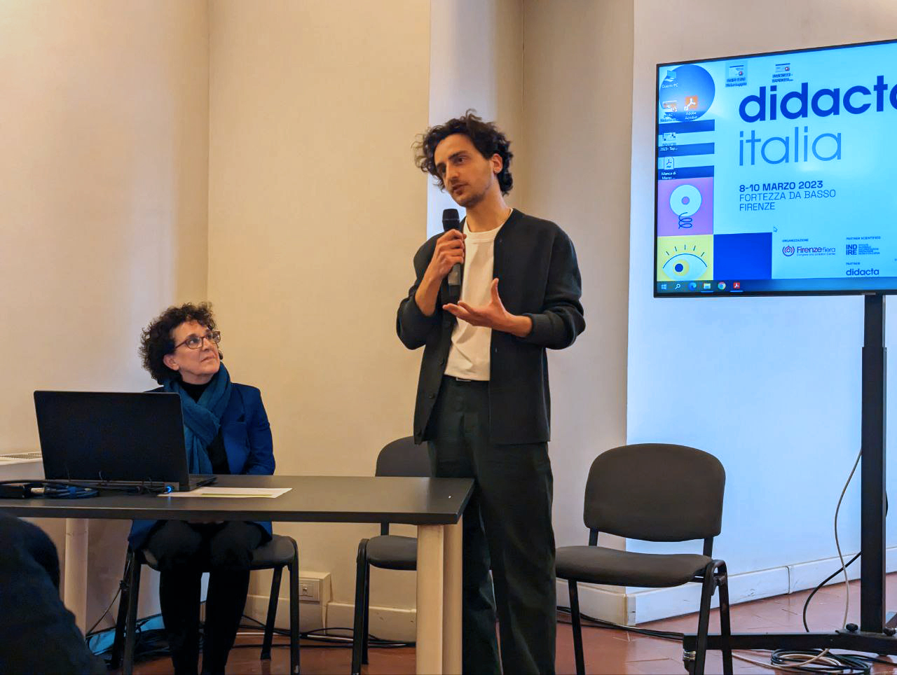Due persone durante una presentazione a Didacta Italia 2023 a Firenze. Un uomo parla al microfono, una donna lo osserva.