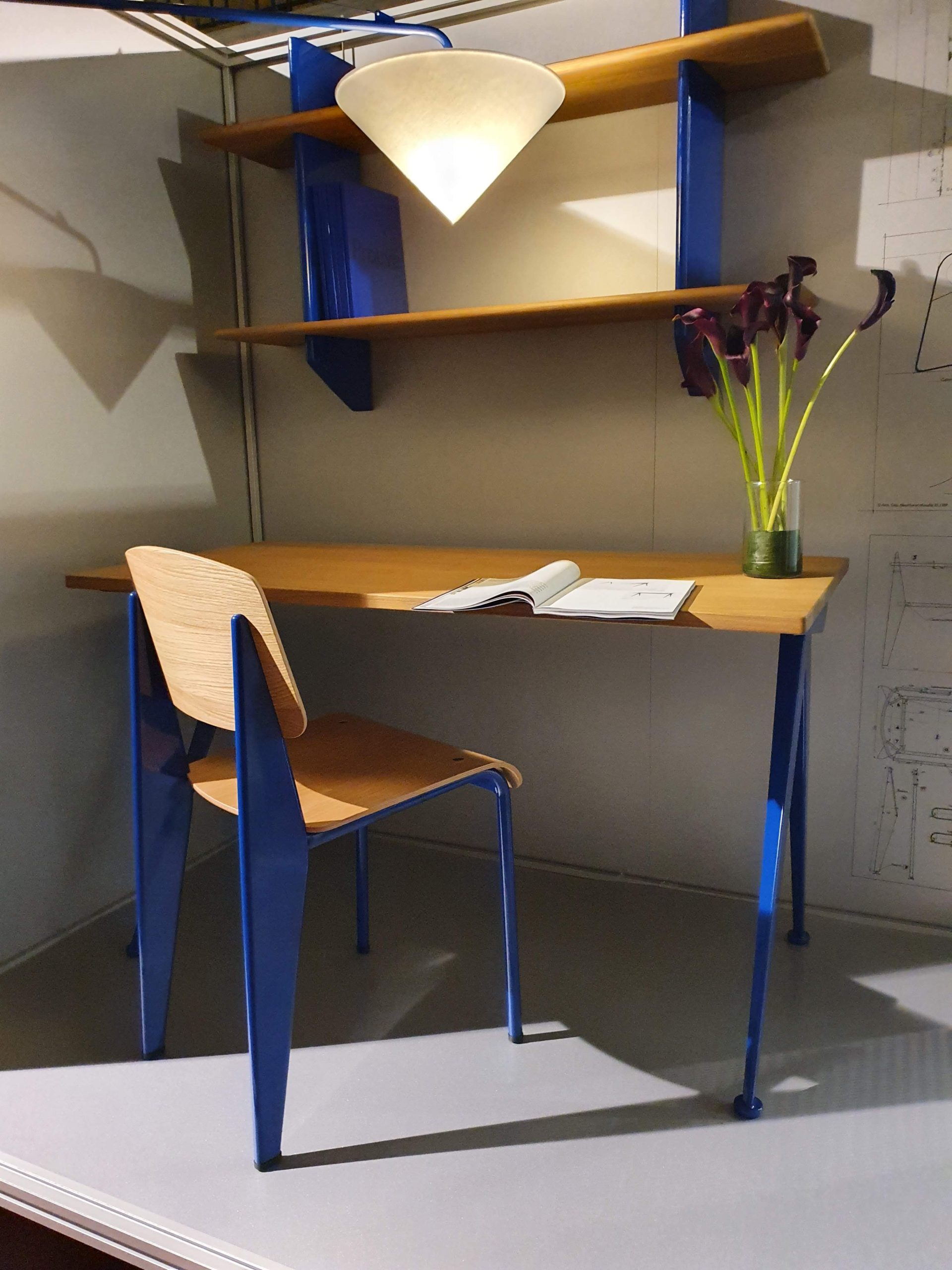 Scrivania moderna con sedia blu, lampada e fiore decorativo, perfetta per un ufficio elegante e funzionale.