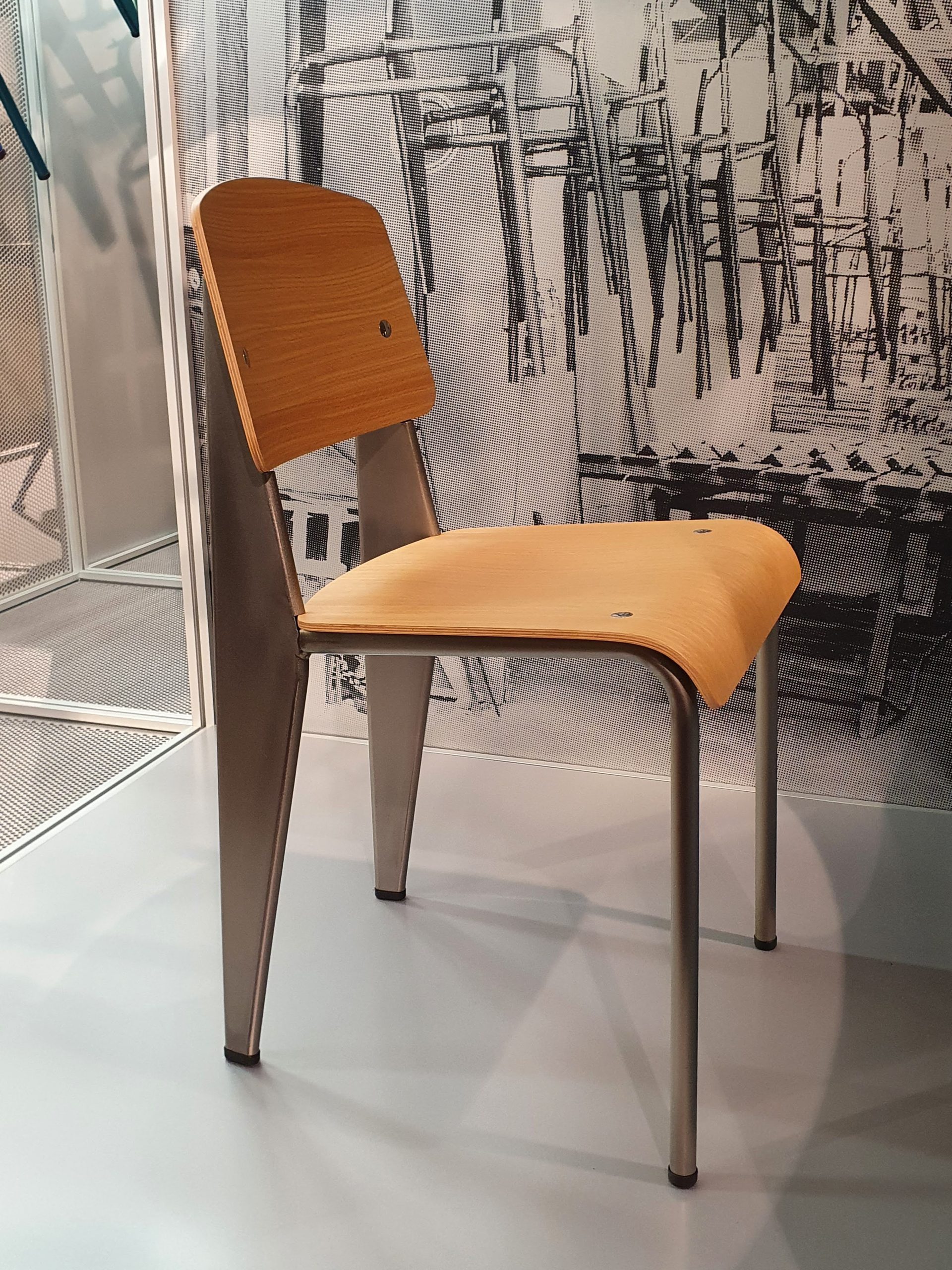 Sedia di design moderno in legno e metallo su sfondo industriale con altre sedie impilate.