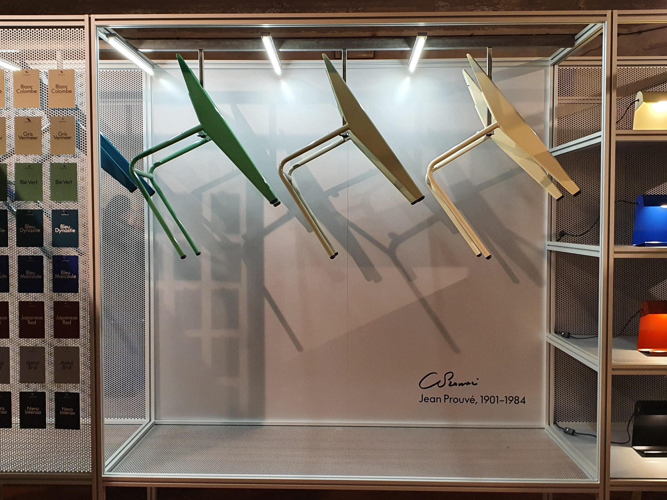Sedie colorate di design di Jean Prouvé esposte in una teca, firma visibile. Palette colori a sinistra.
