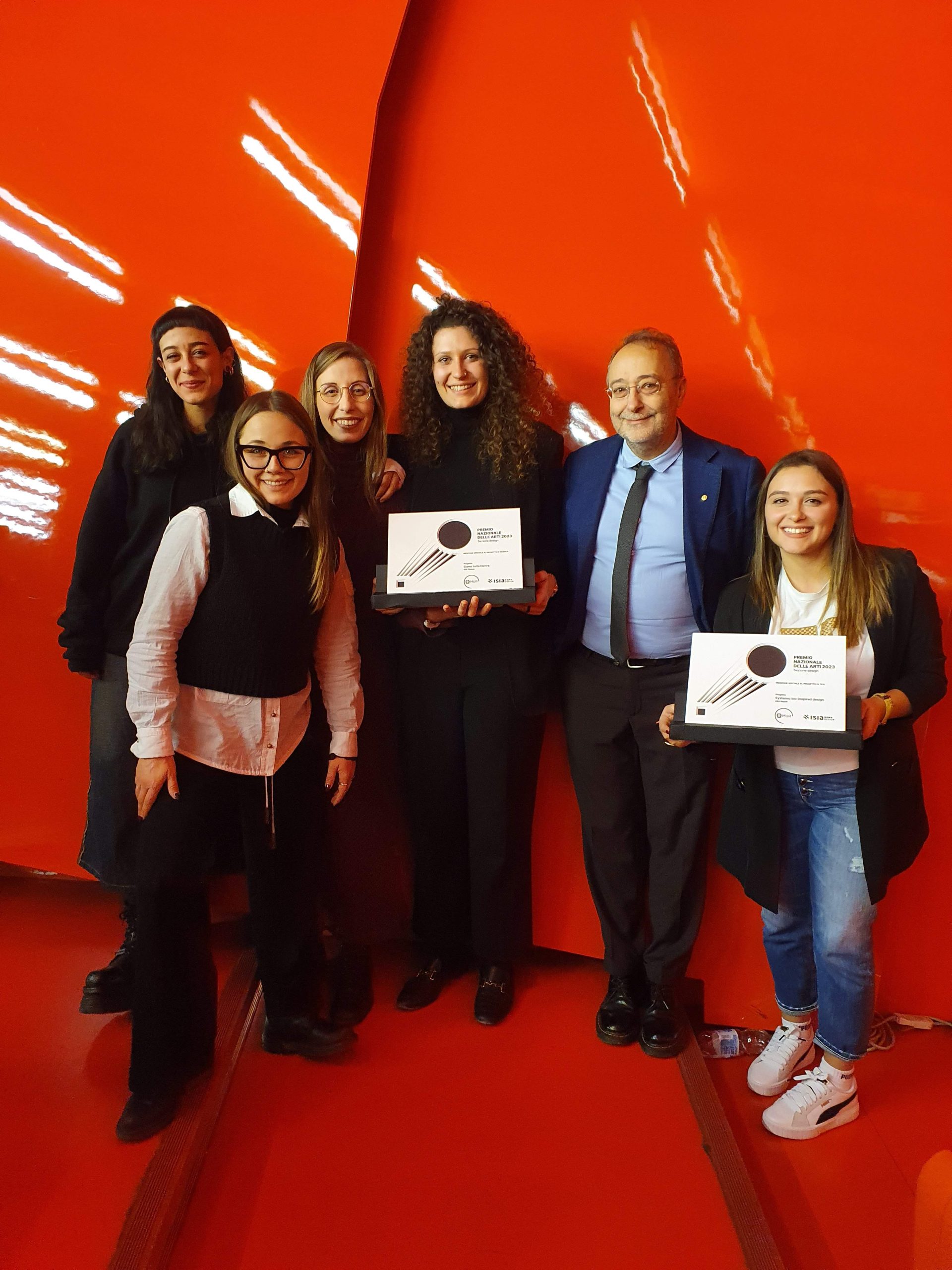 Gruppo sorridente con premi in mano, davanti a uno sfondo rosso brillante.