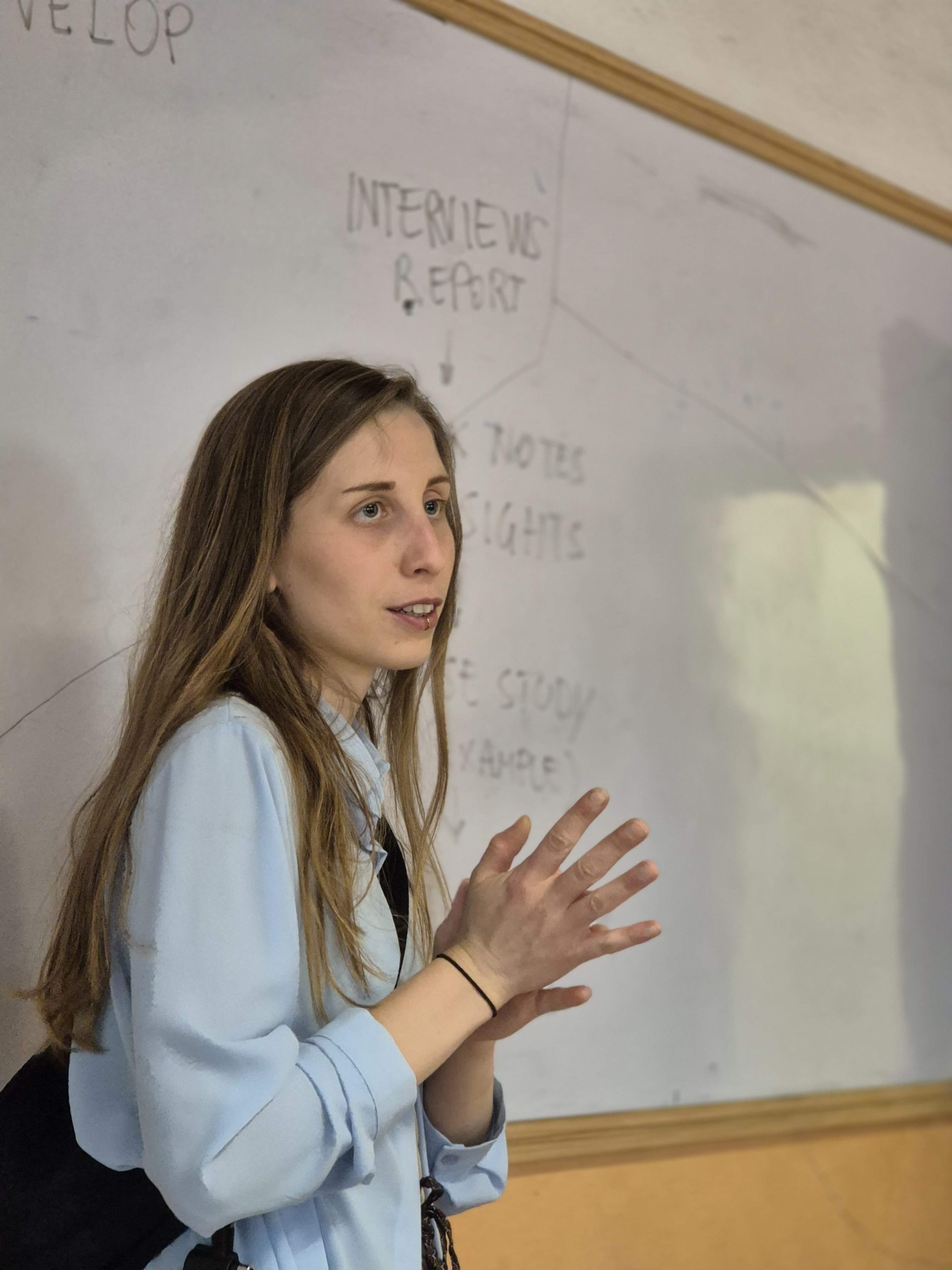 Una donna presenta in aula davanti a una lavagna scritta con appunti di un'intervista.