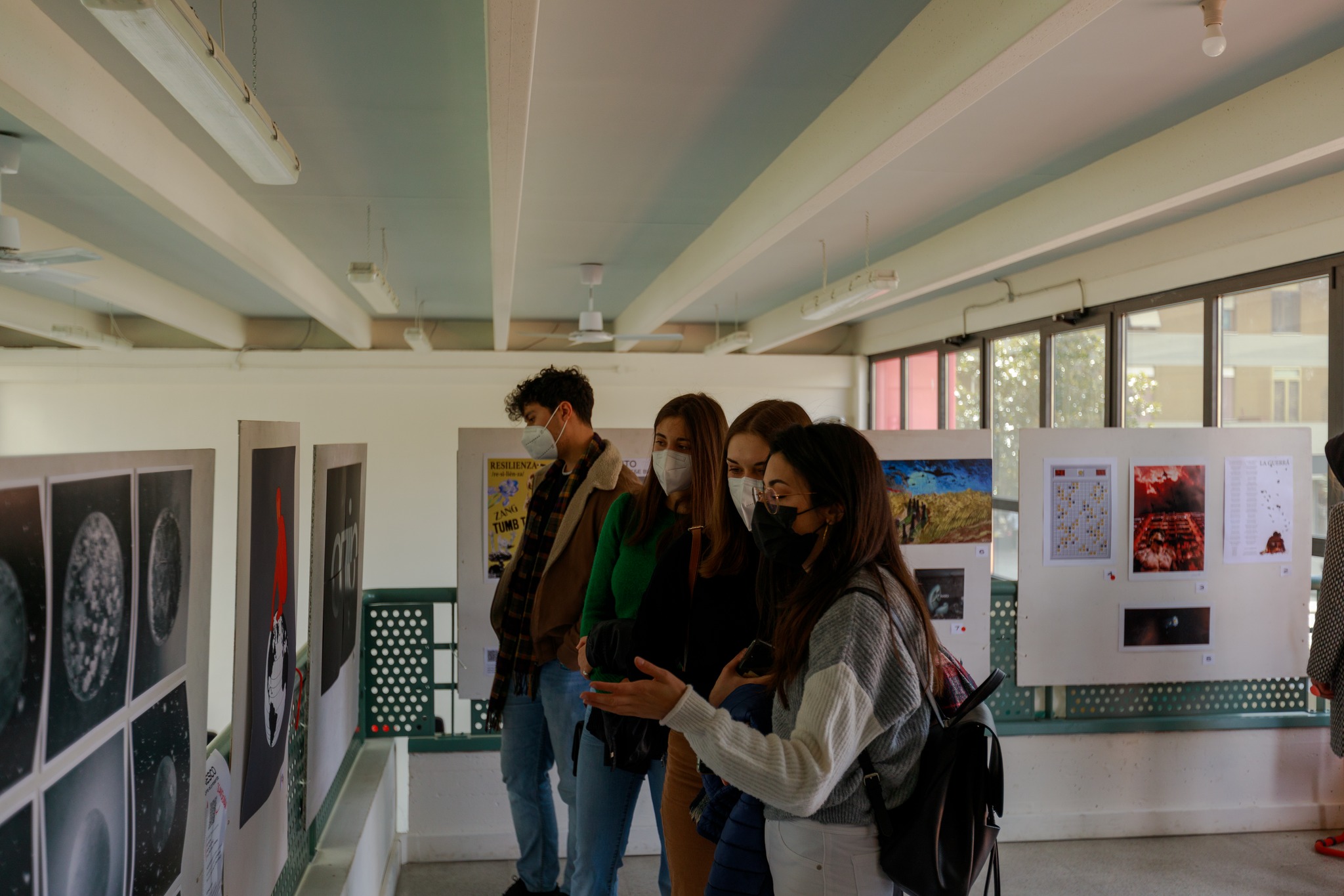 Visitatori con mascherine osservano una mostra fotografica indoor su pannelli espositivi.