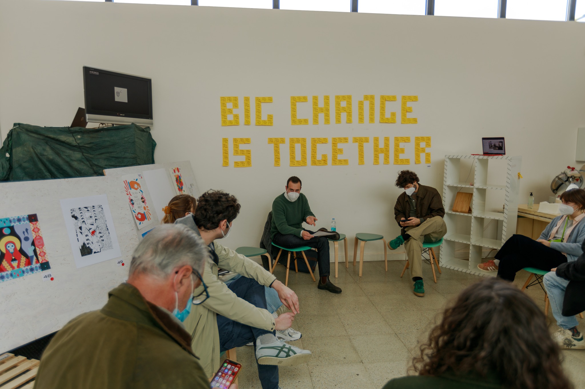 Gruppo di persone in una sala con opere d'arte e un cartello giallo: Big Change Is Together.