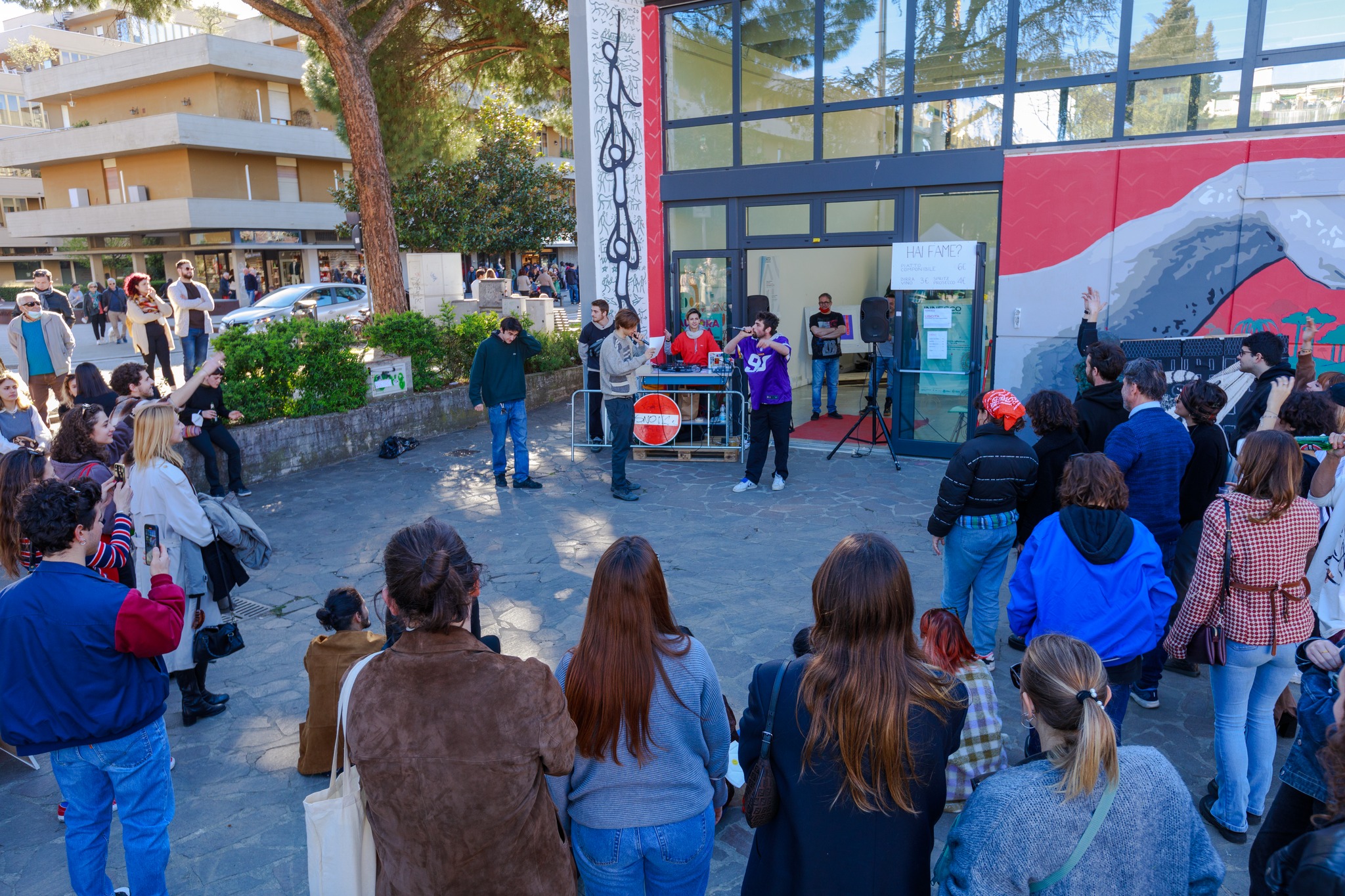 Raduno di persone all'aperto durante un evento con musica dal vivo e spettatori attenti in una giornata di sole.