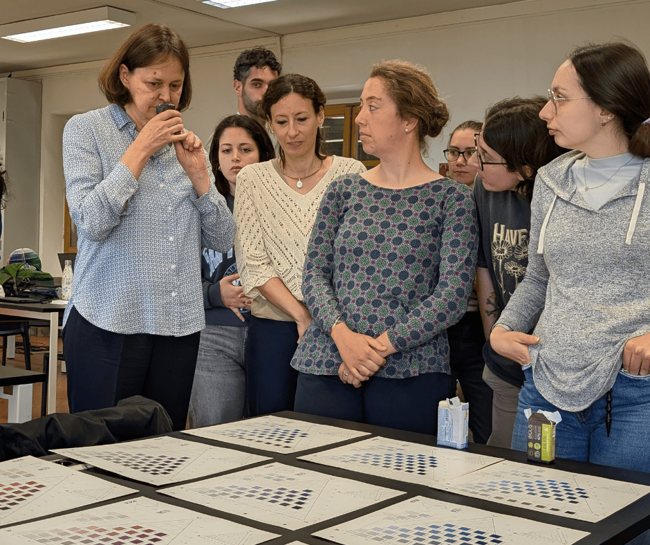 Un gruppo di persone esamina cartelle di colori in un laboratorio, con una donna che osserva attentamente attraverso una lente.
