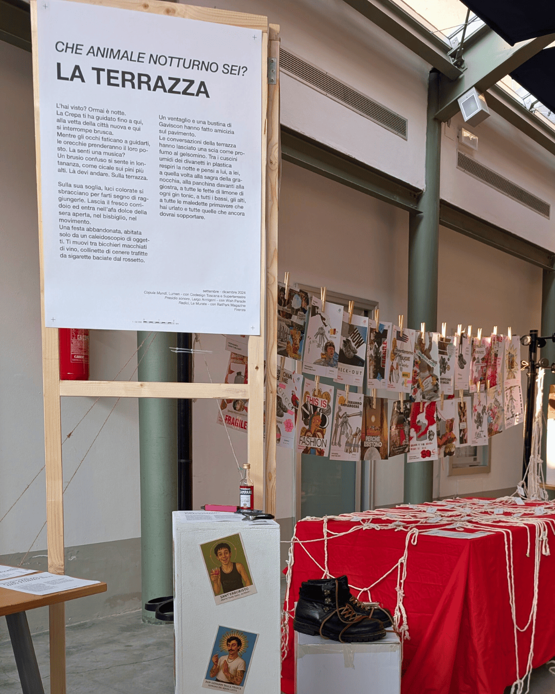 Immagine di un'esposizione artistica interna con un pannello informativo e stampe appese su un filo.