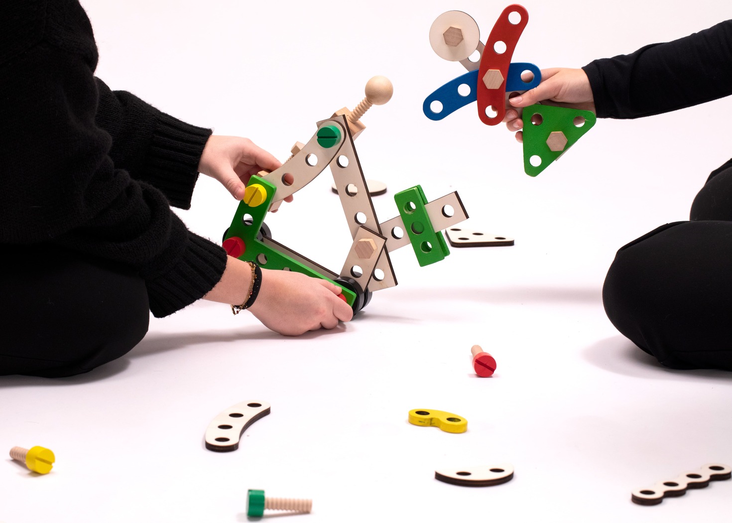 Bambini che giocano con un set di costruzioni in legno, creando strutture colorate su un pavimento bianco.