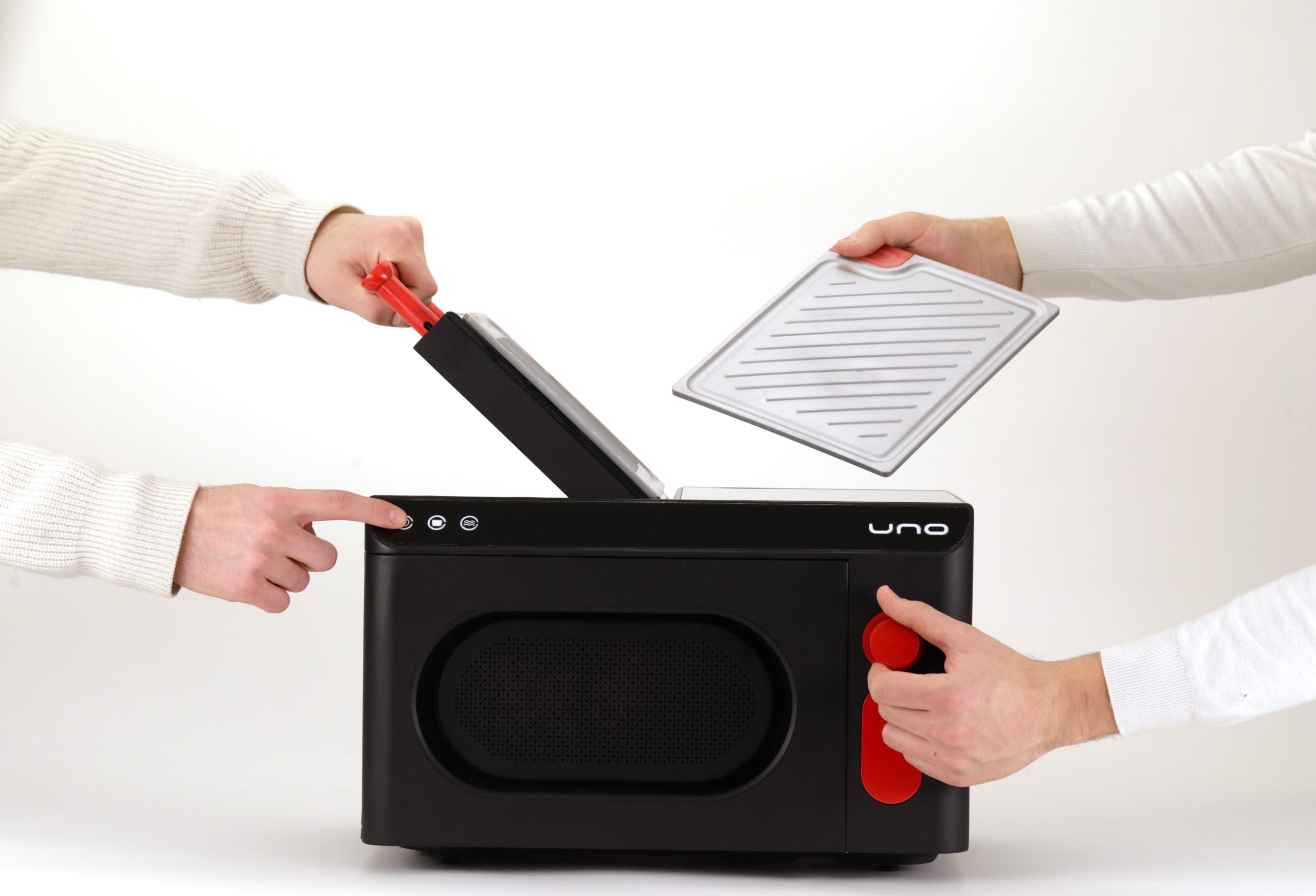 Due persone che utilizzano un dispositivo nero simile a un forno con manopole rosse e coperchio rimovibile.