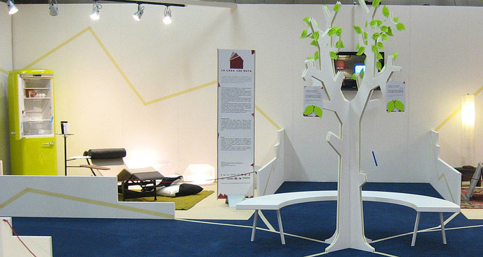 Esposizione moderna con arredamento minimalista, frigo verde e installazione artistica a forma di albero al centro.