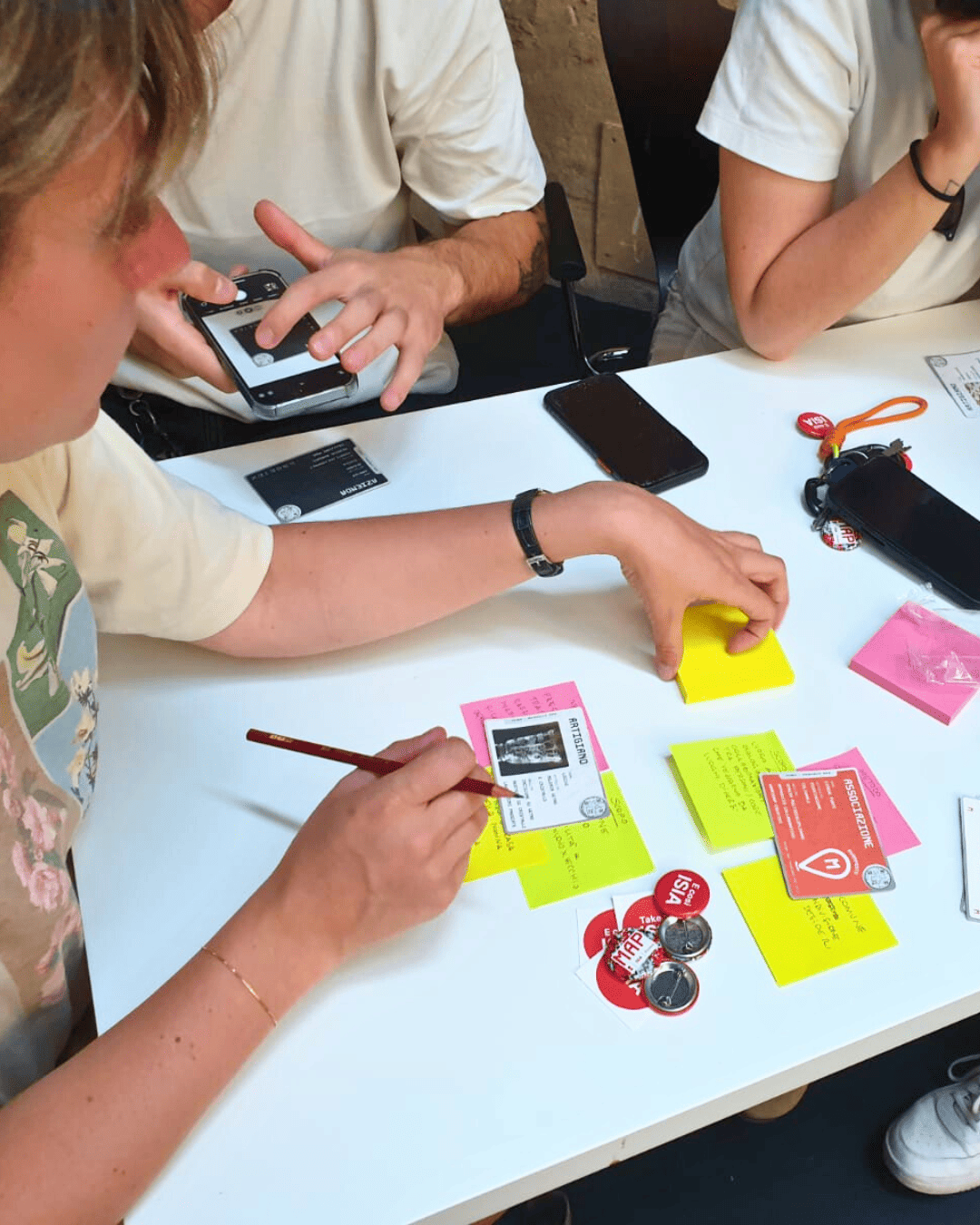 Persone che scrivono su post-it colorati durante una sessione di brainstorming creativo attorno a un tavolo bianco.