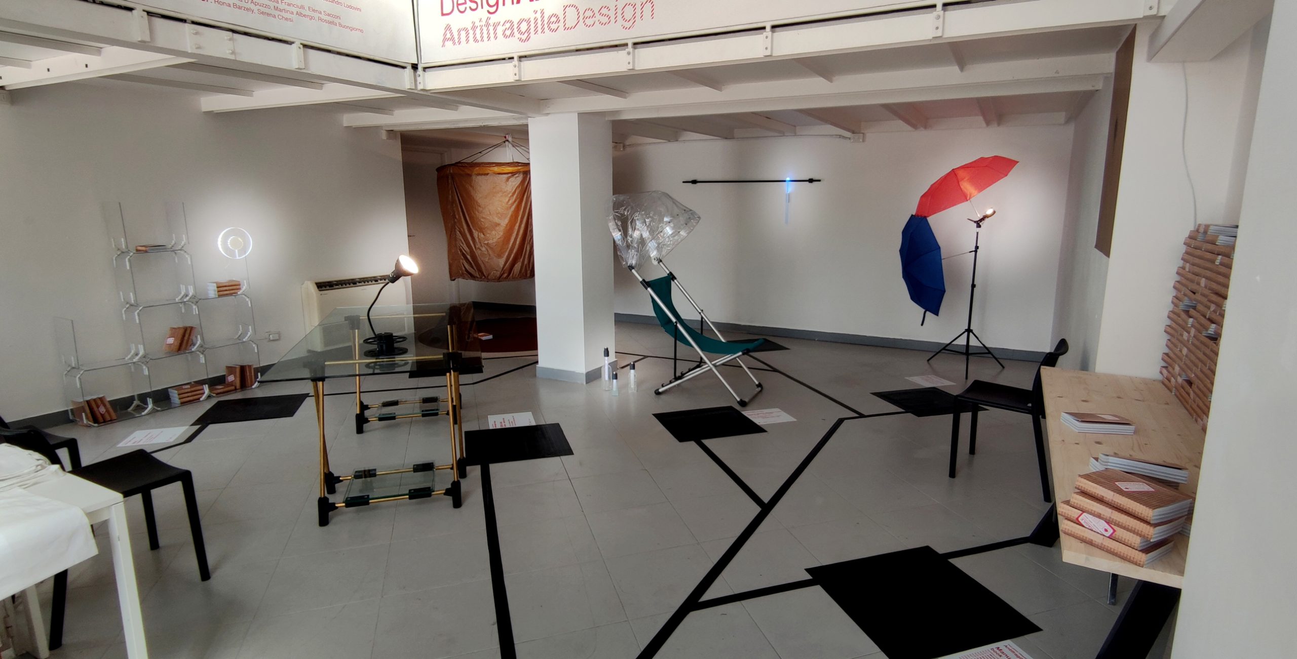 Spazio espositivo di design con arredi moderni, ombrello colorato, lampade e libri su un tavolo in legno.