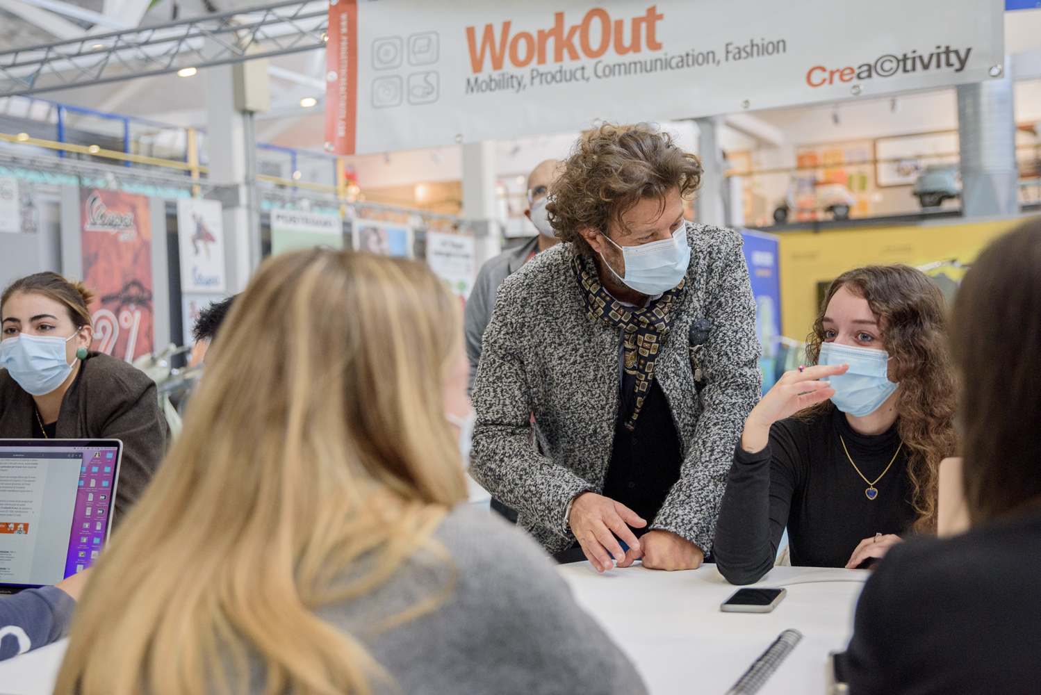 Le persone con mascherine discutono in un workshop di comunicazione creativa al WorkOut, scambiando idee innovative.