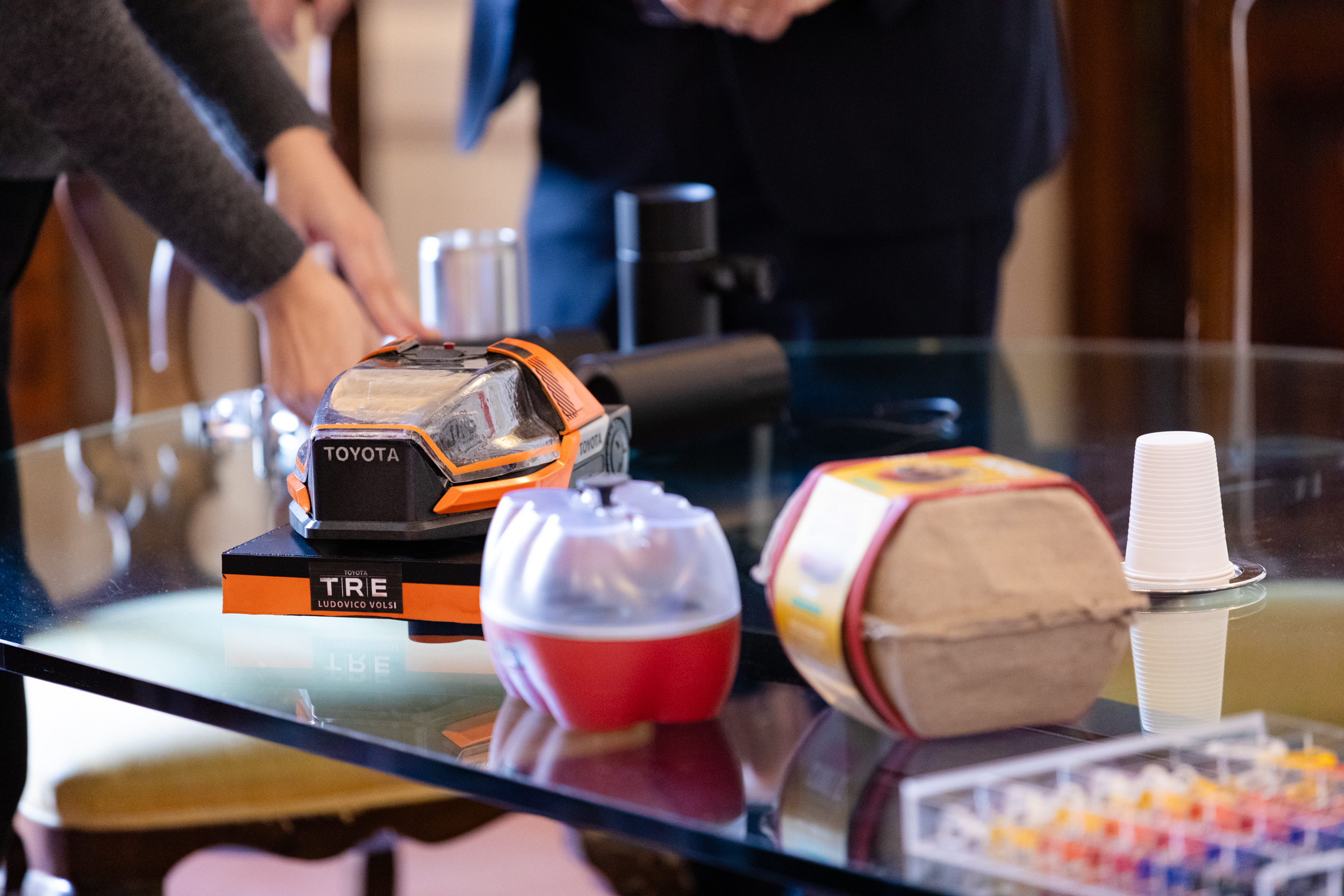 Mani posano prototipo di un modello Toyota su un tavolo pieno di oggetti diversi.