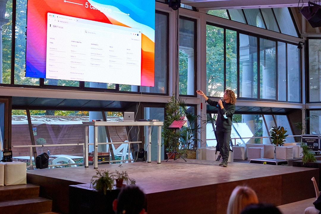 Persona che spiega davanti a un grande schermo con una presentazione in una sala moderna e luminosa.