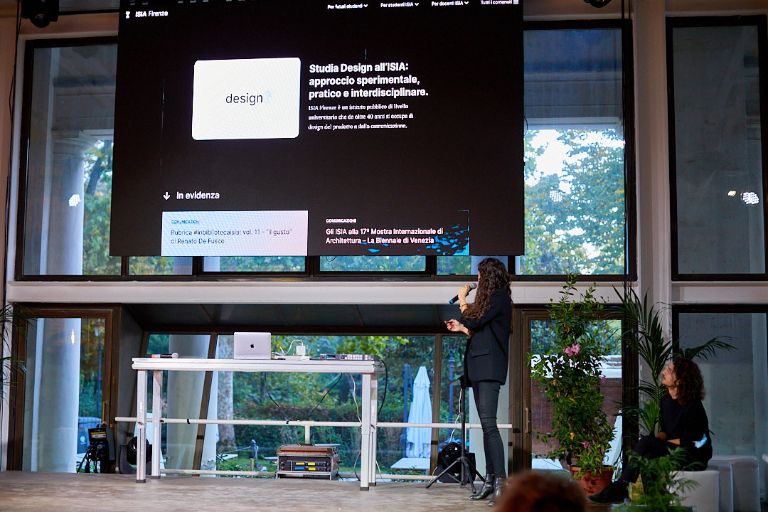 Presentazione su design interdisciplinare all'ISIA con schermo grande e relatrice in piedi accanto al palco.