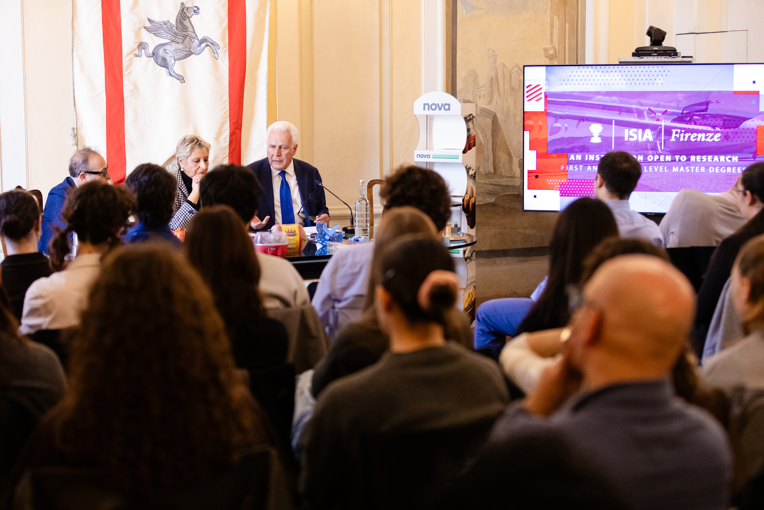 Conferenza accademica all'ISIA Firenze, relatori discutono davanti a un pubblico attento, schermo con grafiche colorate.