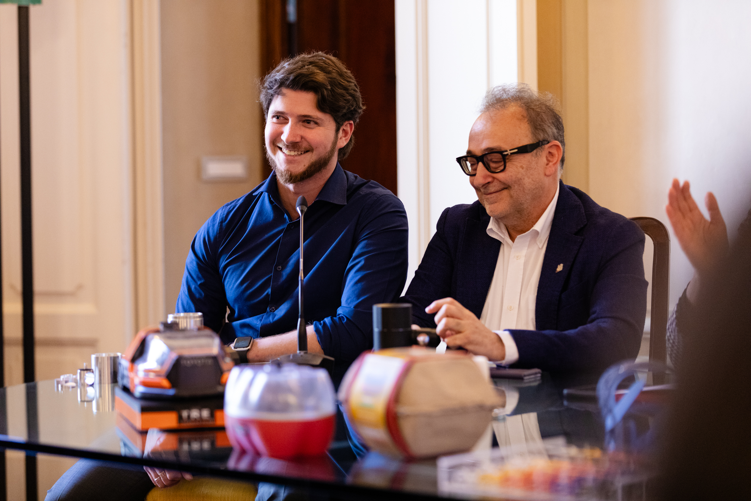 Due uomini sorridenti seduti a un tavolo durante una riunione o conferenza in una sala.