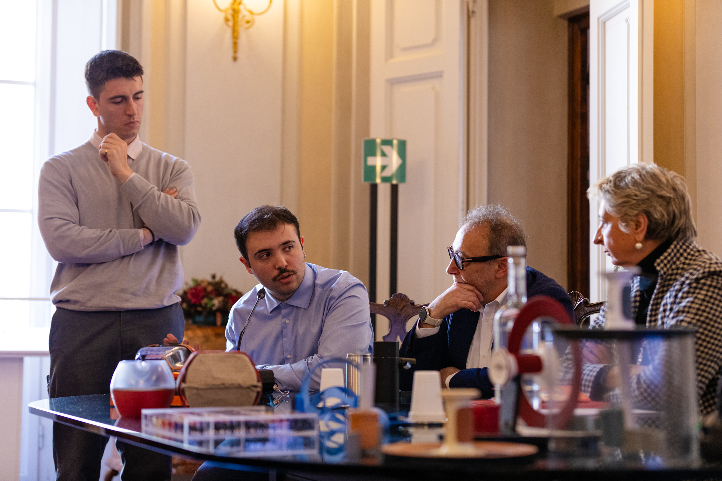 Persone conversano attorno a un tavolo in una sala conferenze elegante, con oggetti vari in primo piano.