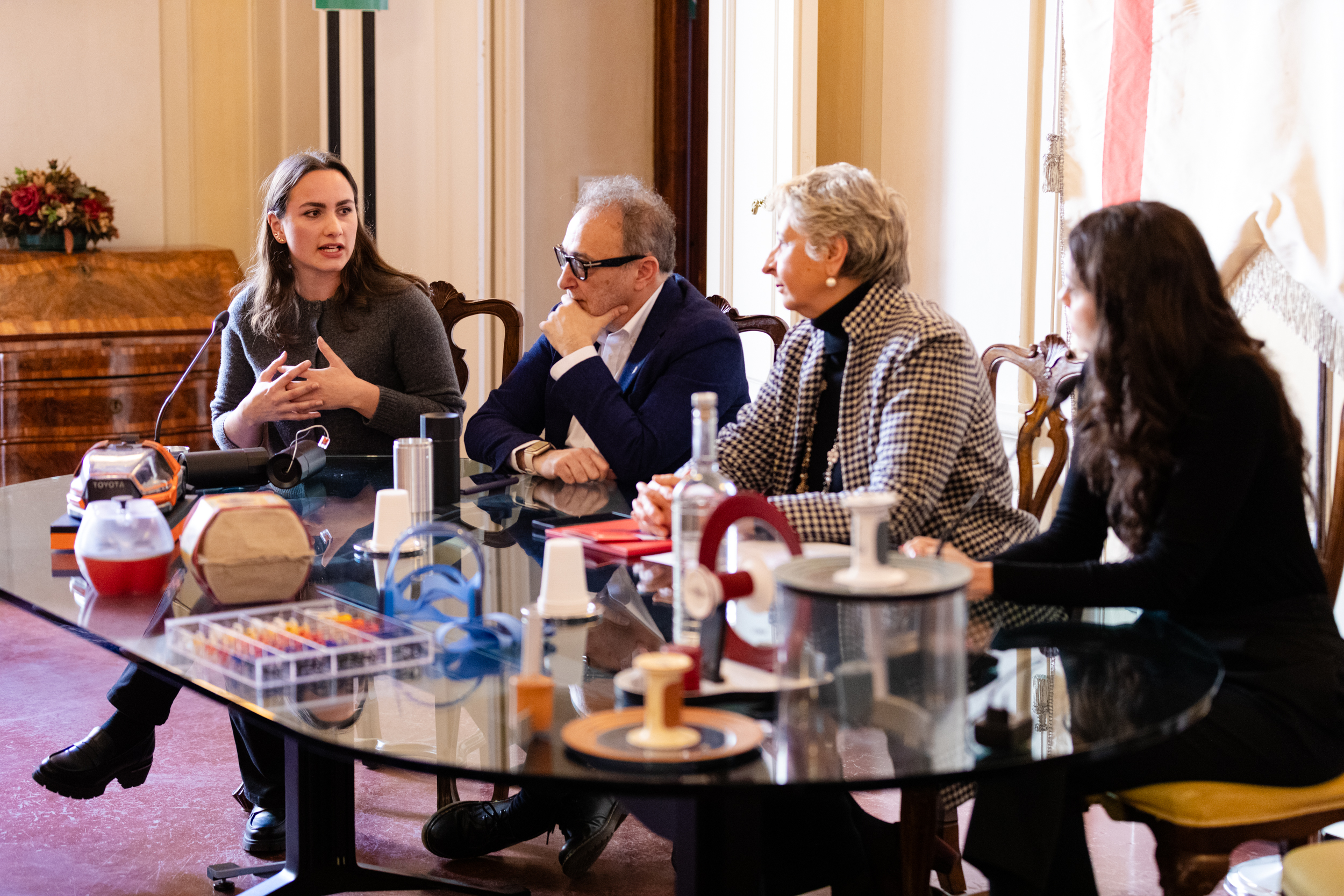 Gruppo di persone in riunione al tavolo, discute di tecnologie con modelli sul tavolo e sedia in legno.