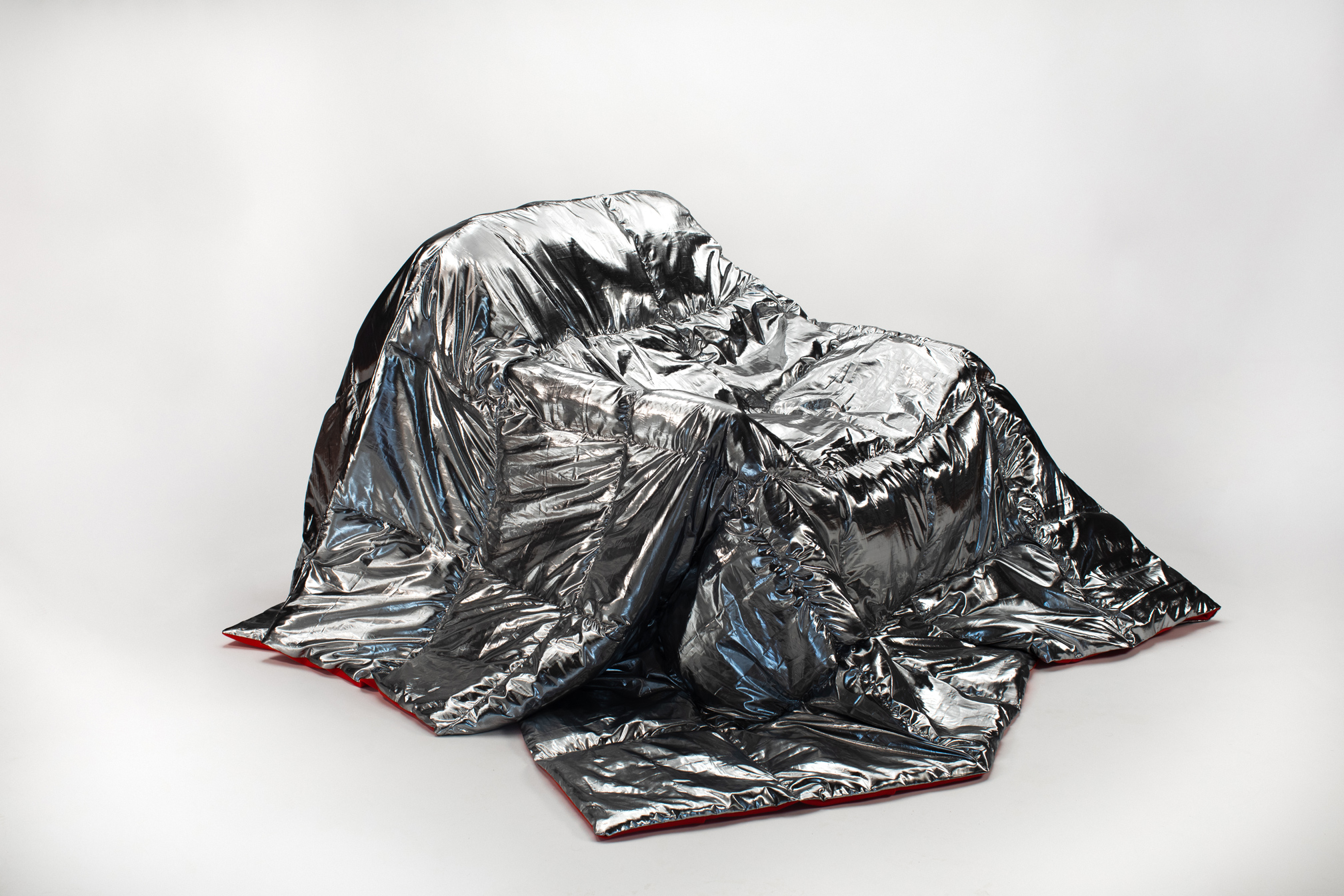 Coperta termica riflettente in alluminio posata su una sedia, su sfondo bianco.