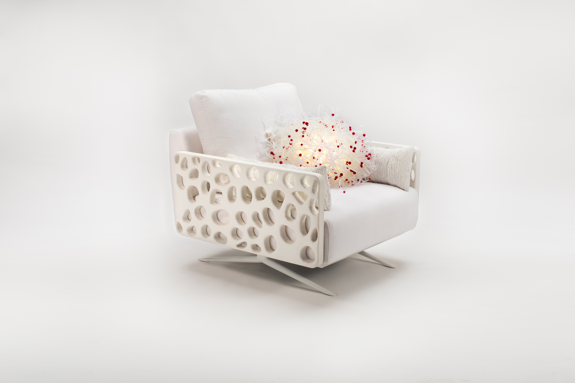 Poltrona bianca moderna con braccioli traforati e cuscini decorativi colorati, su sfondo neutro.