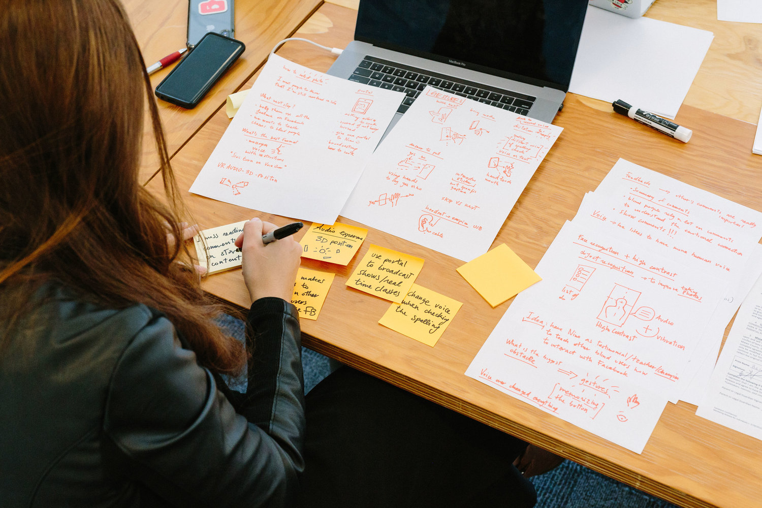 Donna al lavoro su appunti scritti a mano e post-it davanti a un laptop su un tavolo di legno.