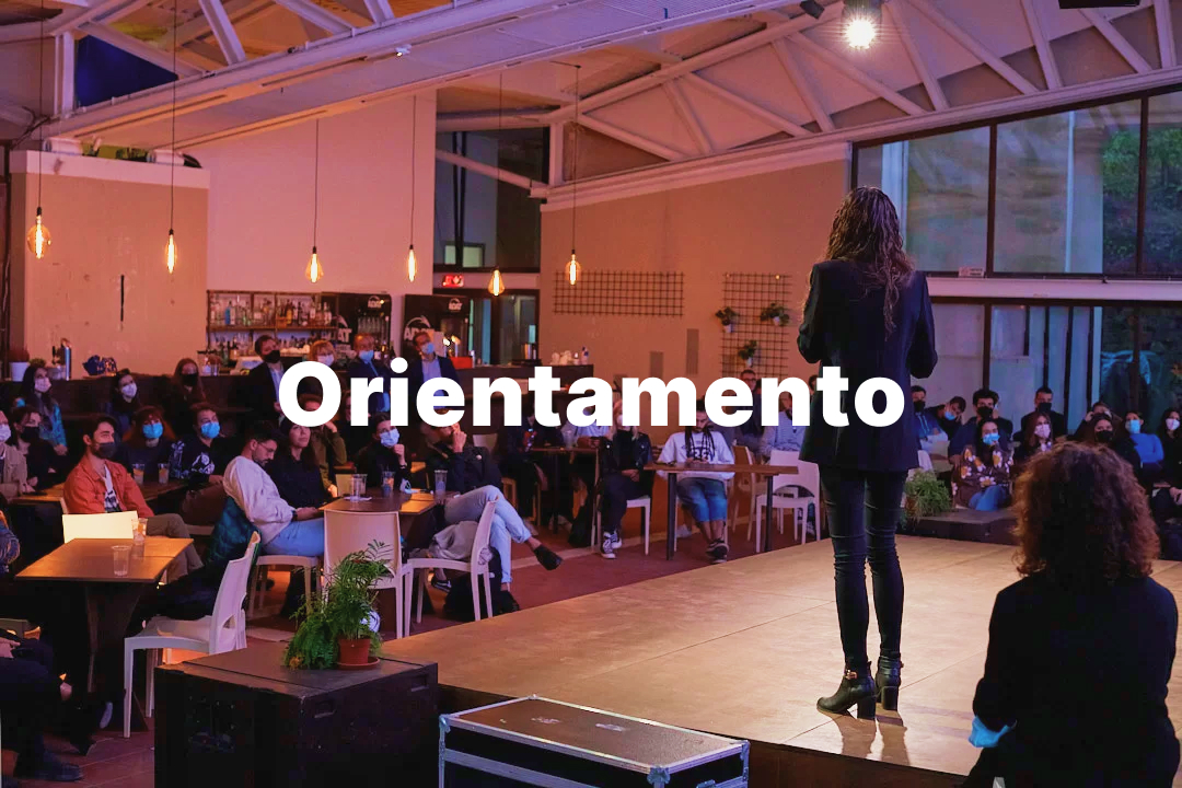 Pubblico seduto ascolta una presentazione su un palco durante un evento di orientamento in un ambiente moderno.