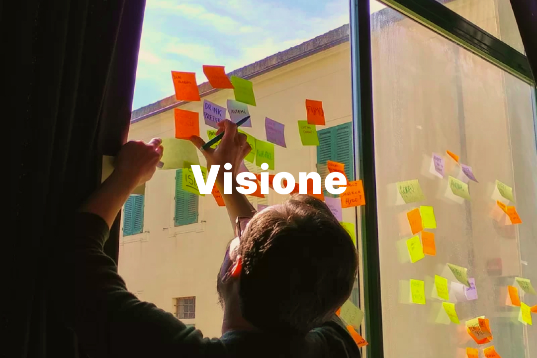 Persona attacca post-it colorati su una finestra, parola Visione sovrapposta, luce naturale.