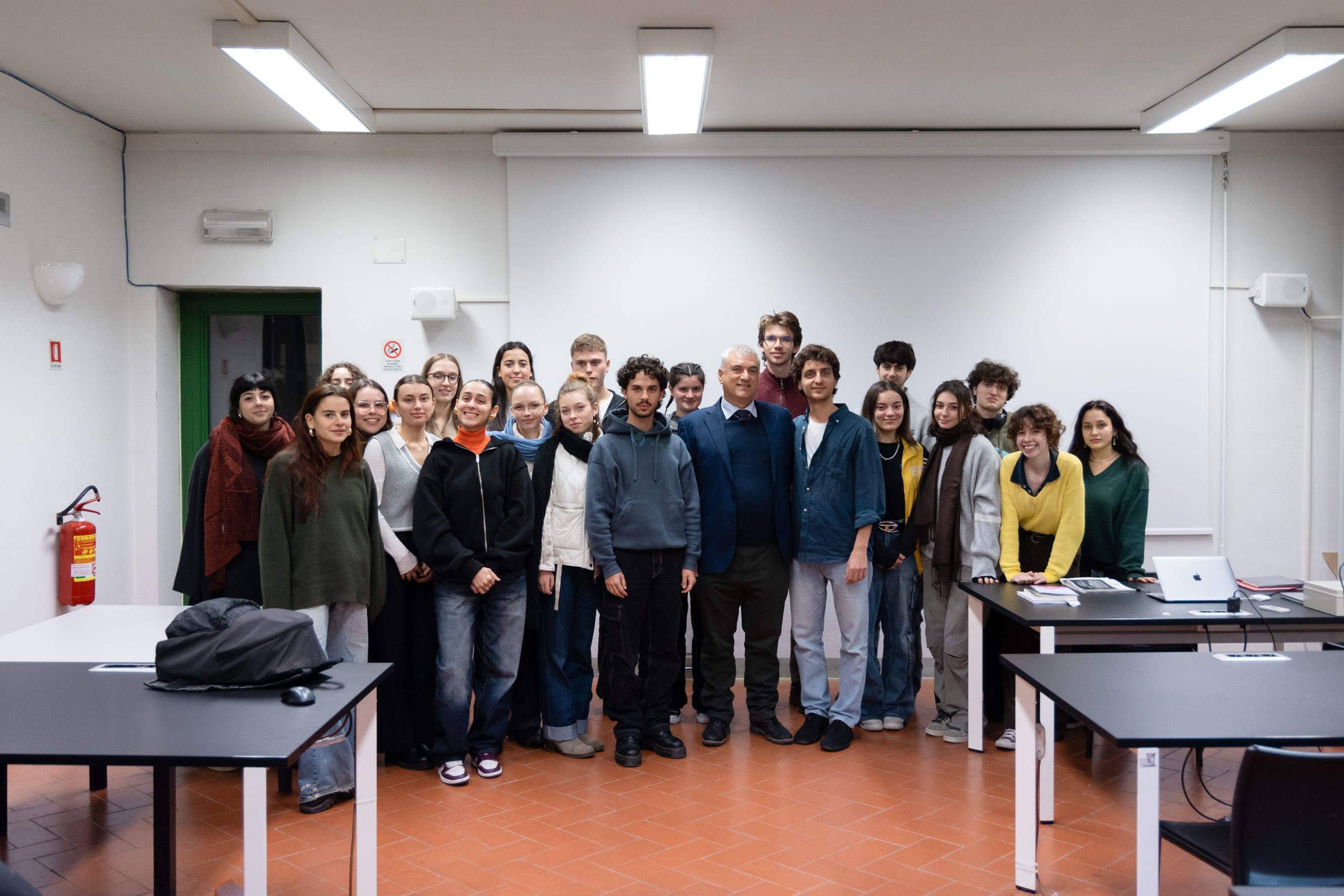 Gruppo di studenti in un'aula universitaria pronti per una lezione, tutti sorridenti e radunati per una foto di gruppo.