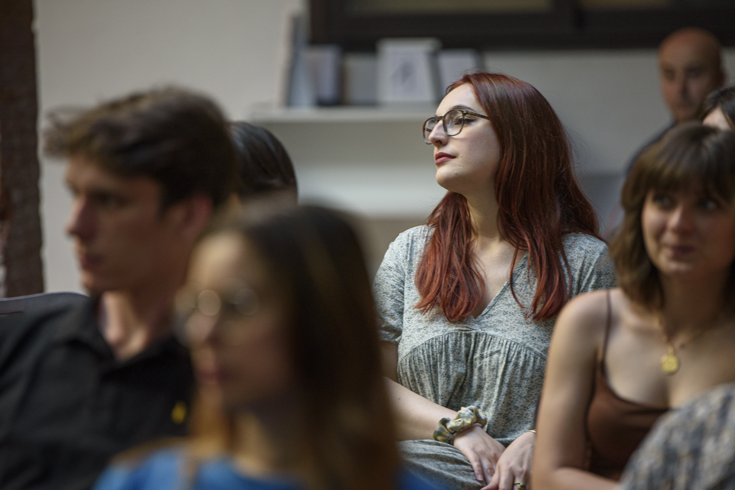 Persone sedute in una sala, alcune con occhiali, ascoltano attentamente una presentazione o conferenza.