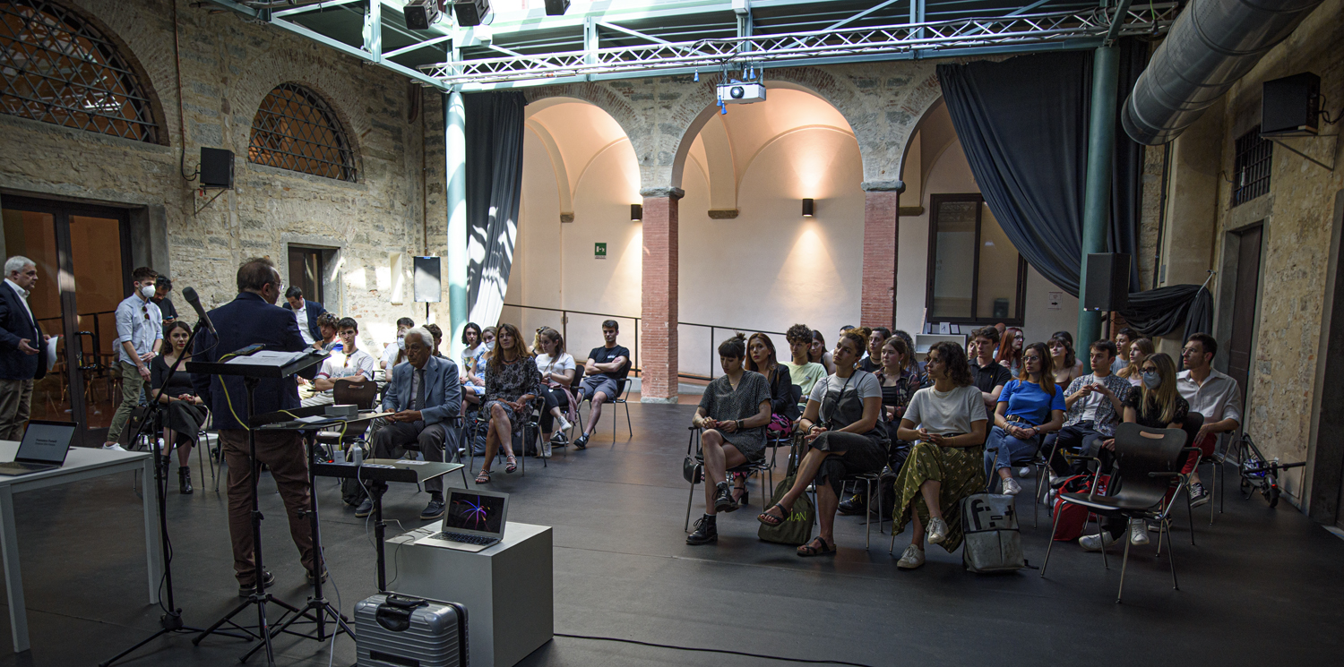 Persone sedute in una sala conferenze con un relatore che parla davanti a un gruppo interessato in un antico edificio.