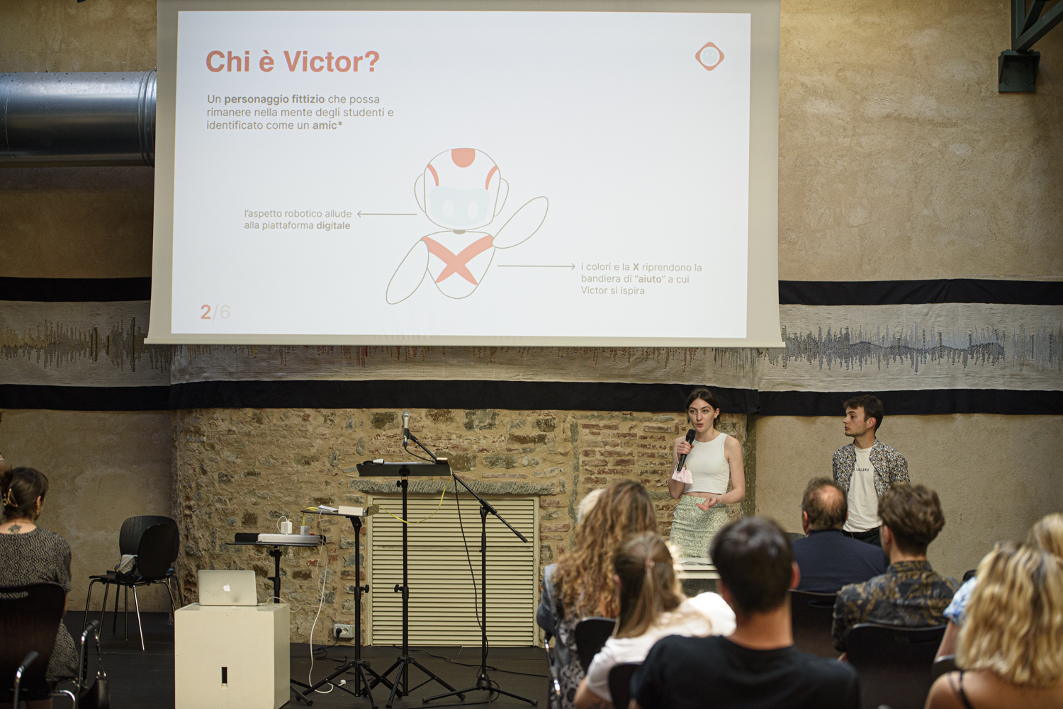 Presentazione su Chi è Victor? con due oratori e un pubblico attento in una sala conferenze.