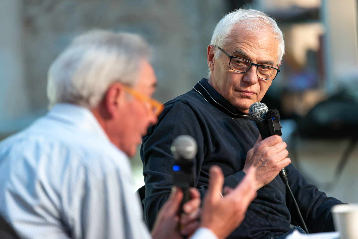 Due uomini anziani discutono animatamente durante un'intervista, entrambi con microfoni in mano.