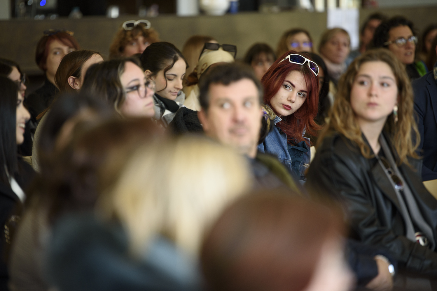 Persone partecipano a un evento, una donna con capelli rossi spicca tra il pubblico attento e variopinto.