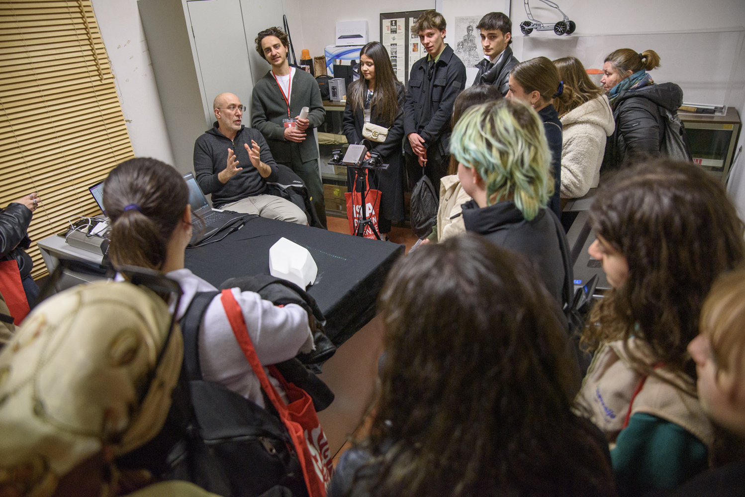 Gruppo di studenti ascolta una lezione in laboratorio, intorno a un tavolo con laptop e modello 3D.