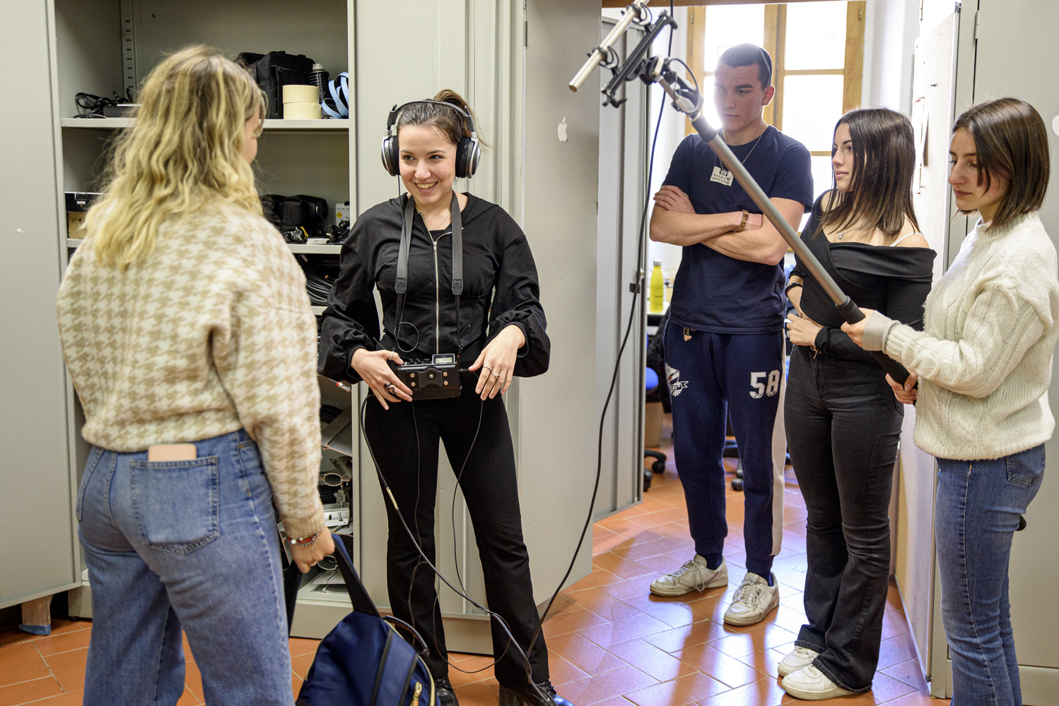Persone in un laboratorio di registrazione audio, una tiene un microfono boom mentre un'altra indossa cuffie professionali.