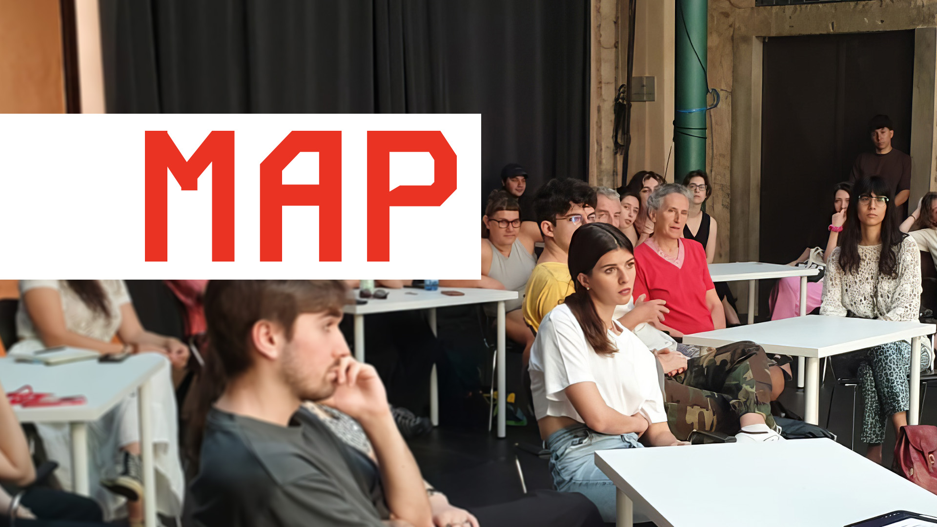 Gruppo di persone sedute ai tavoli durante un incontro, con il logo MAP sovrapposto in rosso.