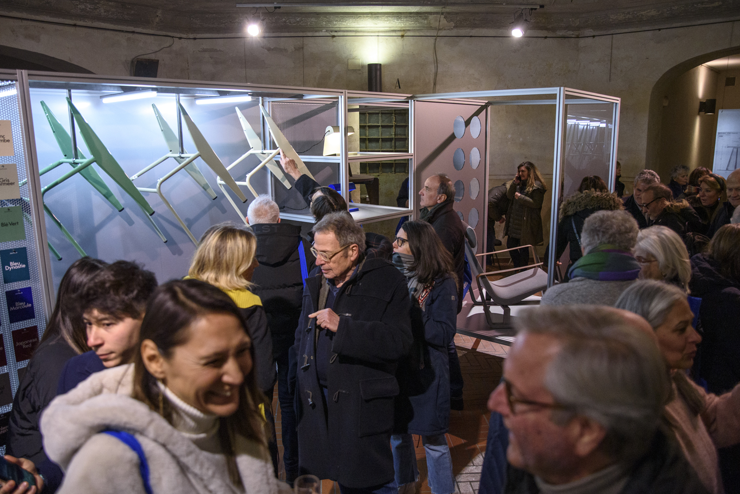 Persone visitano una mostra di design con sedie innovative in esposizione, ambiente affollato e vivace.